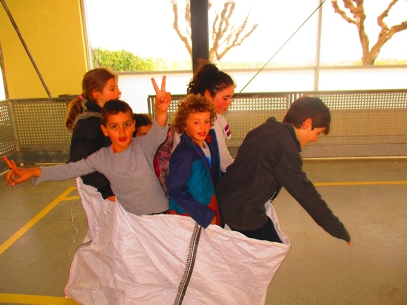 Infants de diferents edats participen plegats en una activitat amb un sac al gimnàs.