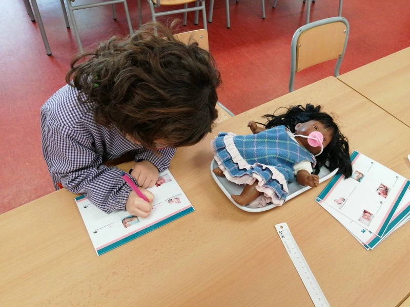 Un infant fa una activitat de llenguatge amb una nina i materials de joc simbòlic.